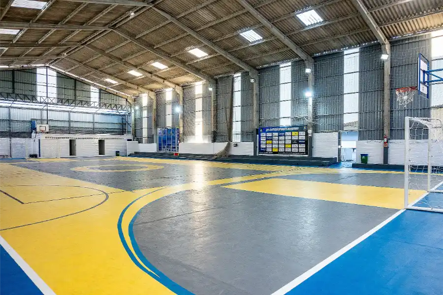 Ginásio poliesportivo do Colégio Atlântico em Itapema, com quadra coberta e piso nas cores azul e amarelo, usado para atividades esportivas e eventos escolares.