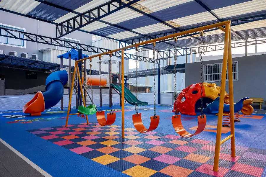 Parque infantil do Colégio Atlântico com escorregadores, balanços e piso emborrachado colorido, projetado para o desenvolvimento e a diversão das crianças da Educação Infantil.